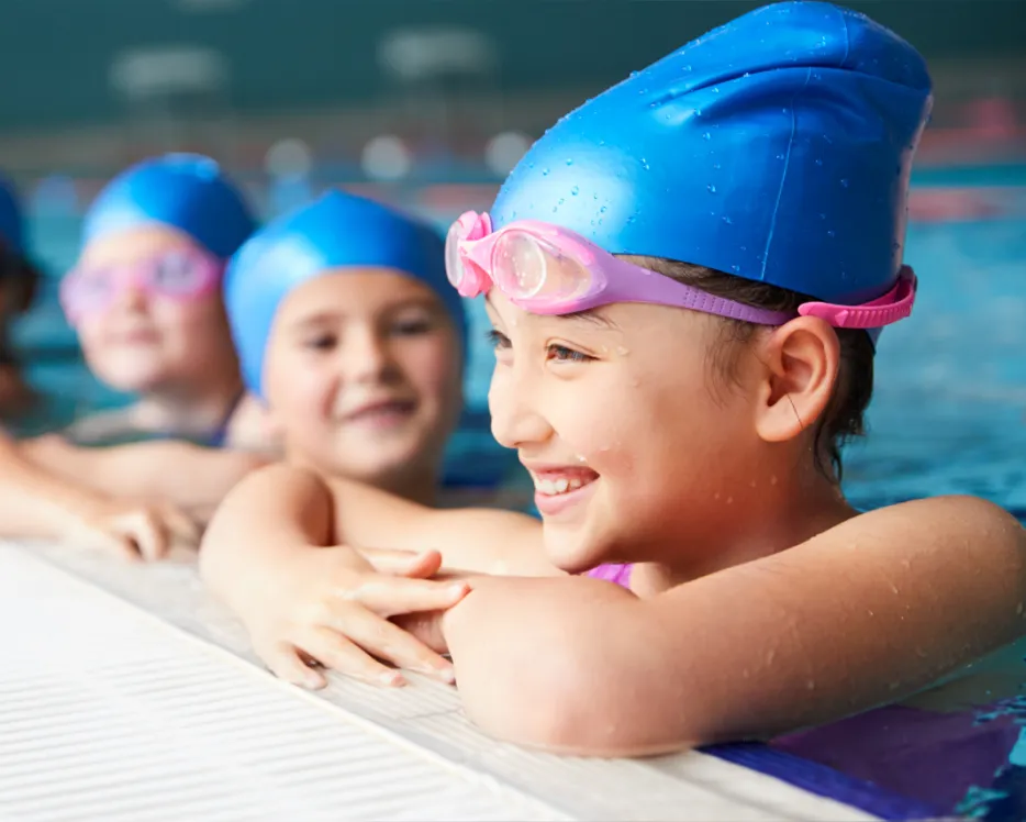 Kinder mit Badekappe halten sich am Rand eines Schwimmerbeckens fest