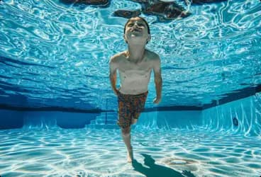 Junge taucht unter Wasser durch ein tiefes Becken